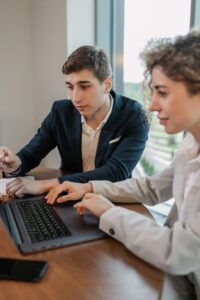 Two young professionals working together on a laptop, discussing projects in a modern office setting.