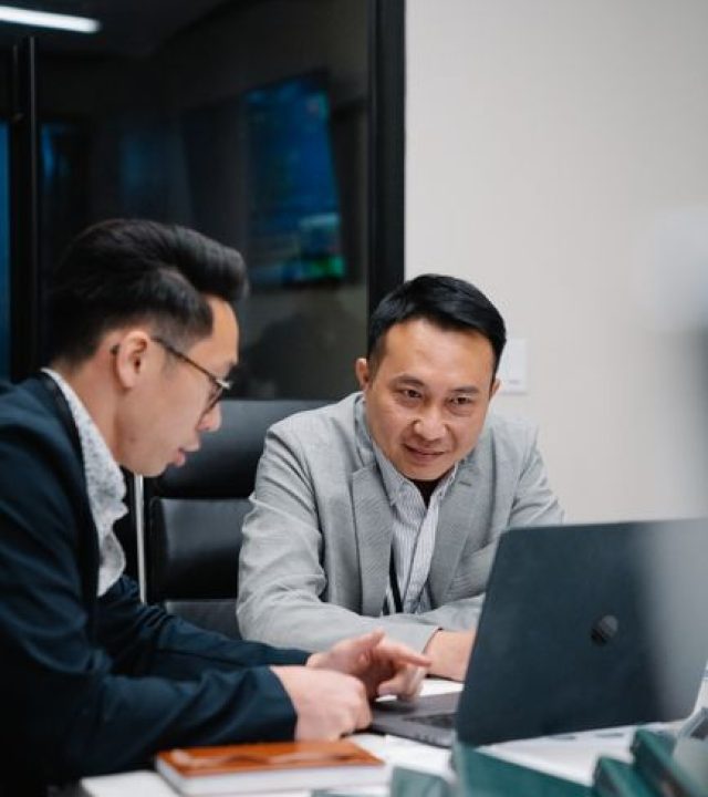 Two men engaged in a business discussion over a laptop in a contemporary office.